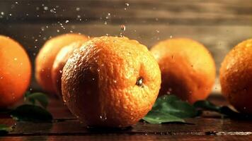 Drops of water with splashes fall on fresh oranges. On a wooden background.Filmed is slow motion 1000 frames per second. High quality FullHD footage video