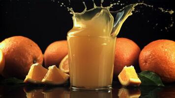 A piece of orange with spray falls into a glass of orange juice. On a black background. Filmed is slow motion 1000 frames per second. video