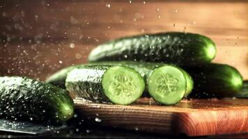 Drops of water with splashes fall on pieces of fresh cucumber. On a wooden background. Filmed is slow motion 1000 frames per second. video