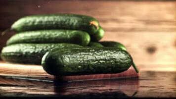 un Fresco Pepino caídas en el mesa con salpicaduras de agua. en un de madera antecedentes. filmado es lento movimiento 1000 marcos por segundo. video