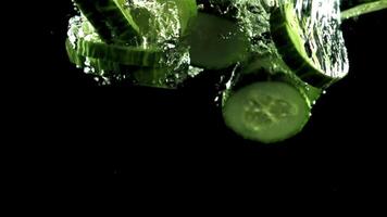 bitar av färsk gurka falla under de vatten med luft bubblor. på en svart bakgrund. filmad är långsam rörelse 1000 ramar per andra. video