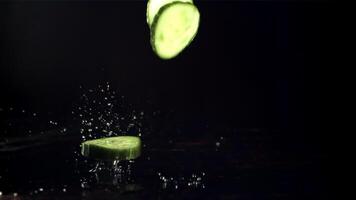 Pieces of fresh cucumber fall on the table with splashes of water. On a black background. Filmed is slow motion 1000 fps. High quality FullHD footage video