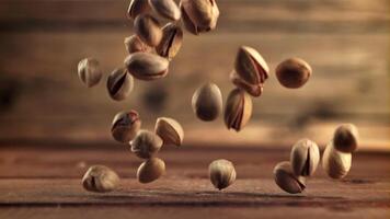 pistachenoten vallen Aan de tafel. Aan een houten achtergrond.gefilmd is langzaam beweging 1000 fps. hoog kwaliteit full HD beeldmateriaal video