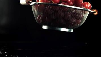 un colador con uvas caídas en el mesa con gotas de agua. en un negro fondo.filmado es lento movimiento 1000 fps. video