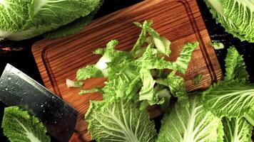 Sliced Beijing cabbage falls on a wooden cutting board. On a black background. Top view. Filmed is slow motion 1000 fps. video