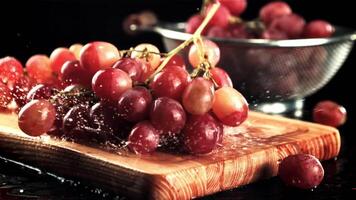 Grapes fall on a cutting board with splashes of water. On a black background. Filmed is slow motion 1000 fps. High quality FullHD footage video