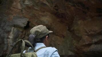 só mulher caminhante com mochila olhando por aí para Vejo a beleza do caverna parede em rochoso montanha durante verão. natureza exploração. hobbies e lazer. paralaxe tomada. video