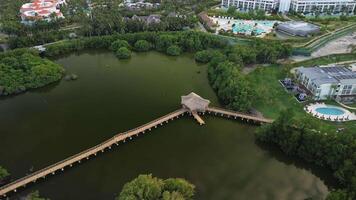 antenne filmische visie vangt cirkelen schot van loopbrug versierd met Prieel, ingelijst door weelderig oerwoud achtergrond, terwijl de zon sets over- rustig meer. tropen. geheimen Koninklijk strand punta cana video