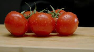 Bright red, beautiful, wet tomatoes are falling onto a cutting board against a black background. Drops of water are splashing off of them. Close up. Slow motion. video