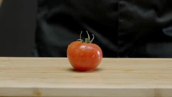 One red tomato is spinning on the chopping board, with drops of water flying off it. Close up. Slow motion. video