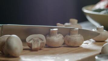 chef cuts several mushrooms in half with a single, swift motion of the knife on the kitchen counter. Close up. Slow motion. video