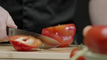 Red ripe bell peppers are sliced in half with a single, well-aimed swing of a large kitchen knife, using the skillful hands of a chef. Close up. Slow motion. video