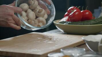 male chef's hands are seen dumping mushrooms onto a table from a large plate on a cutting board in a restaurant kitchen, with an abstract background. Close up. Slow motion. video