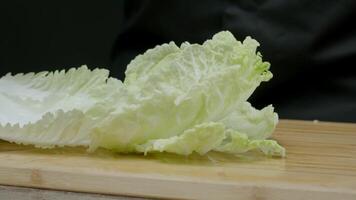 washed green leaf of chinese cabbage falls onto a wooden cutting board, and drops of water from it splash in all directions. Close up. Slow motion. video