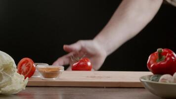 One tomato falls onto the chopping board, among the other vegetables that are lying on the table. Splashes of water fly everywhere. The tomato rolls off the table and the cook catches it. Close up. Slow motion. video