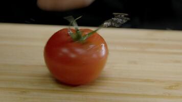 de koken voorzichtig spins een sappig rood tomaat Aan de hakken bord, en druppels van water vlieg uit het. dichtbij omhoog. langzaam beweging. video