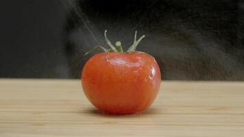 1 vermelho tomate é pulverizado com água a partir de uma spray garrafa, tão este gotas do água fluxo baixa isto para tiroteio. fechar acima. lento movimento. video