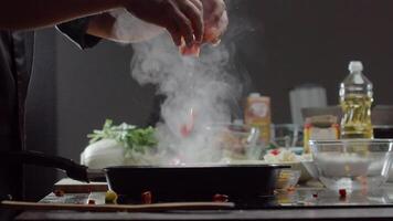 cocineros masculino manos lanzar un rebanado tomate dentro un caliente fritura pan a crear un delicioso vegetal guiso. cerca arriba. lento movimiento. video