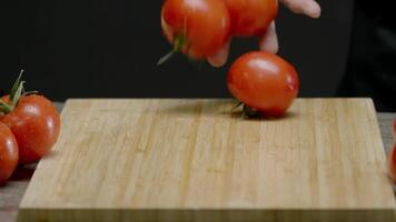 wooden cutting board with washed tomatoes rolling on it against an abstract background is seen in the camera's view. Close up. Slow motion. video