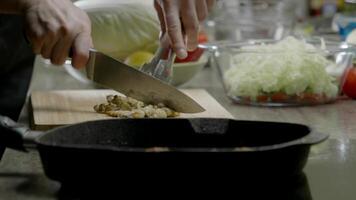 cuisinier est Coupe poulet Viande dans le Restaurants cuisine, lequel est ensemble contre une toile de fond de une friture poêle. proche en haut. lent mouvement. video