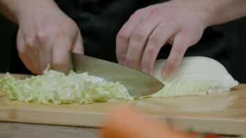 chefe de cozinha fatias chinês repolho com uma faca em uma corte borda em uma Preto fundo. comovente Câmera. fechar acima. lento movimento. video