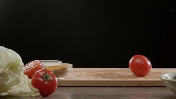 Few juicy and ripe red tomatoes drop onto the chopping board, among other vegetables that are lying on the table. Splashes of water fly around as they land. Close up. Slow motion. video