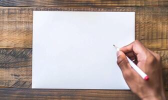 A hand holding a graphite pencil poised over a blank sheet of white paper photo