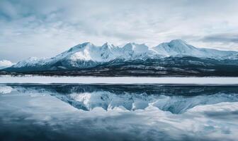 A distant view of snow-capped mountains reflected in the frozen surface of a lake photo