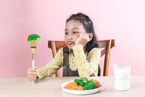 asiático pequeño linda niña se niega a comer brócoli sano vegetales. foto