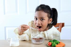 linda pequeño asiático niña comiendo chocolate cereal foto