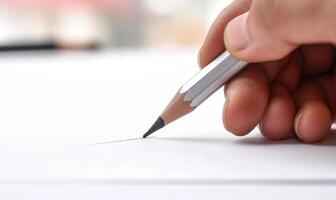 A hand holding a graphite pencil poised over a blank sheet of white paper photo