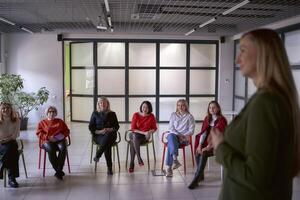 un mujer con largo pelo en un verde chaqueta en escenario, colegas escuchando desde el salón foto