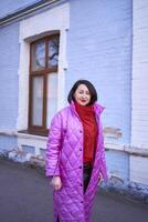 a stylish woman in a long bright pink, magenta coat and red shoes walks the streets of the city photo