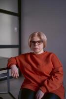 portrait of a woman with a disability in an orange sweater and leather pants in the office photo