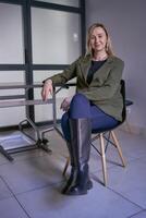 blonde woman with long hair in a green jacket and jeans in the office photo