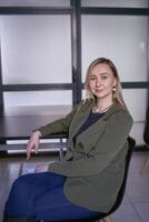 blonde woman with long hair in a green jacket and jeans in the office photo