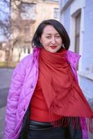 a stylish woman in a long bright pink, magenta coat and red shoes walks the streets of the city photo