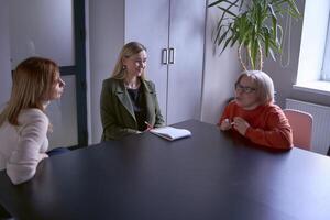 Tres mujer, incluso un persona con un discapacidad, discutir el de la empresa estrategia a un reunión en el oficina foto