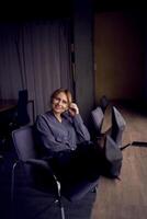 hermosa mujer en negocio ropa se sienta en un moderno oficina, piernas en tacones de aguja arrojado en el mesa foto