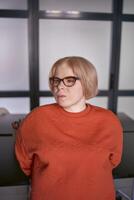 portrait of a woman with a disability in an orange sweater and leather pants in the office photo