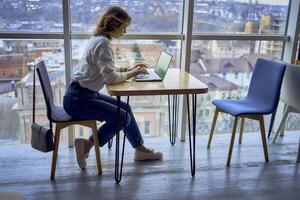 middle age woman working on a laptop in a coworking space with panoramic windows and a view of the city from above, laptop with a green screen, Chroma key photo