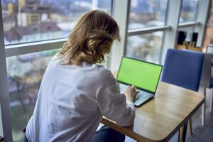 middle age woman working on a laptop in a coworking space with panoramic windows and a view of the city from above, laptop with a green screen, Chroma key photo