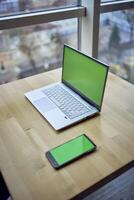 ordenador portátil y teléfono con verde pantalla en soltero lugar de trabajo mesa, croma llave, foto