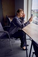 beautiful middle age business woman wearing gray shirt, wide leg pants and black stilettos fix her hair looking into phone camera in modern workspace photo