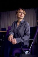 beautiful middle age business woman wearing gray shirt, wide leg pants abd black stilettos sit in purple office chair in modern workspace photo