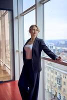 attractive middle age woman in jacket and white t-shirt posing in modern office with panoramic windows photo