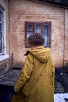 woman in yellow coat in front of brick building photo