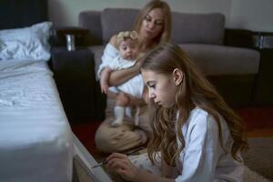 girl paint on the floor while her mother plays with baby sister photo