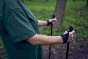 mayor mujer es comprometido en nórdico caminando con palos en el primavera bosque foto