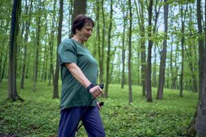 mayor mujer es comprometido en nórdico caminando con palos en el primavera bosque foto